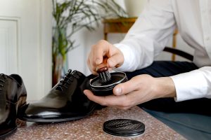 Męskie dłonie nakładające pastę do butów skórzanych Cocciné na eleganckie ciemne buty (tzw. lotniki)
