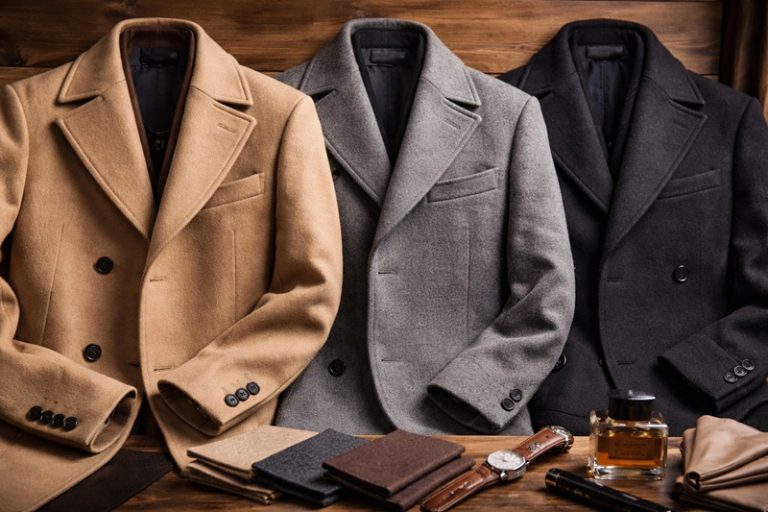 Eleganckie płaszcze męskie z różnych materiałów ułożone na drewnianej powierzchni, obok akcesoria modowe podkreślające styl i jakość wykonania